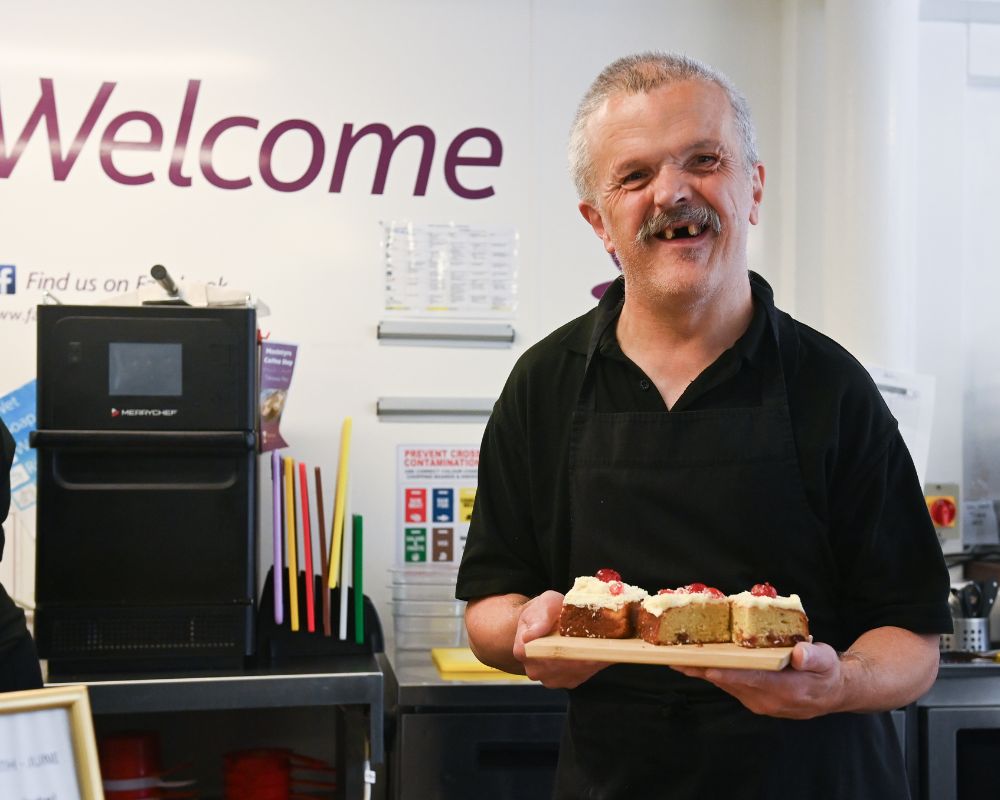 Man holding cakes in front of a Welcome sign at a cafe
